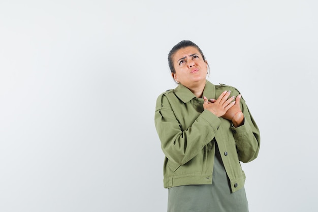 Femme tenant les mains sur le coeur en veste, t-shirt et à la recherche anxieuse.