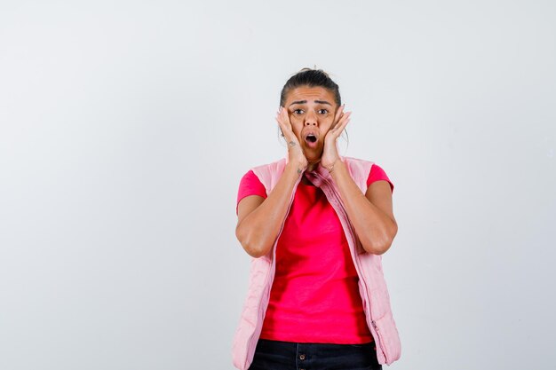 Femme tenant les mains sur les joues en t-shirt, gilet et choquée