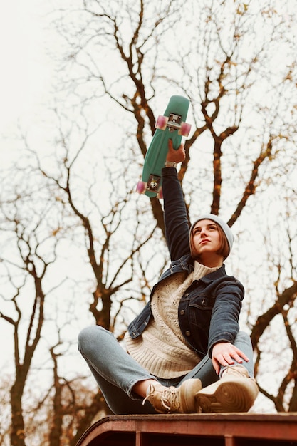 Photo gratuite femme tenant une planche à roulettes en position assise