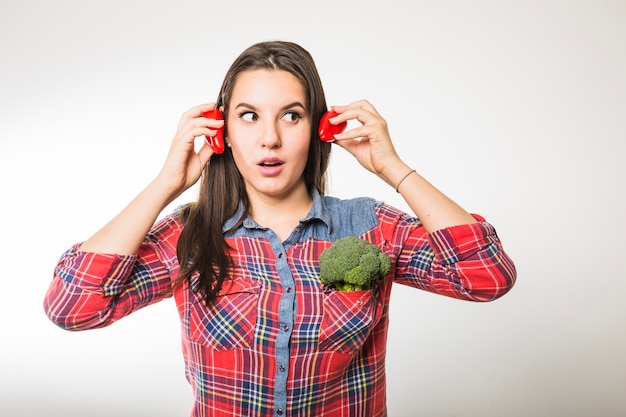 Femme tenant des poivrons près des oreilles