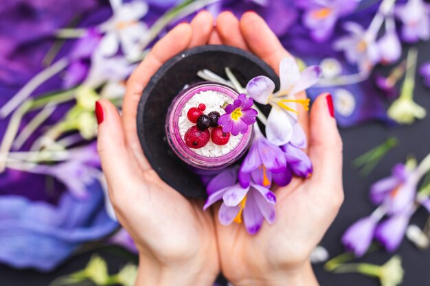 Femme tenant un pot de smoothie végétalien garni de baies, entouré de fleurs