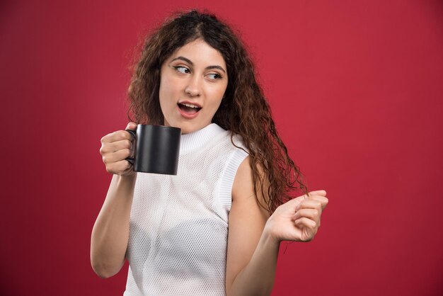 Femme tenant une tasse noire chaude sur le rouge