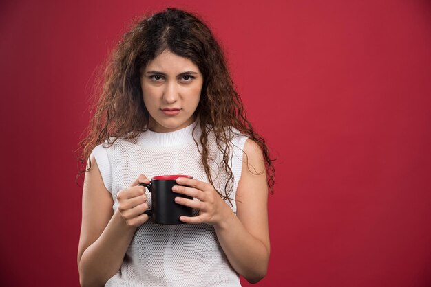 Femme tenant une tasse noire chaude sur le rouge