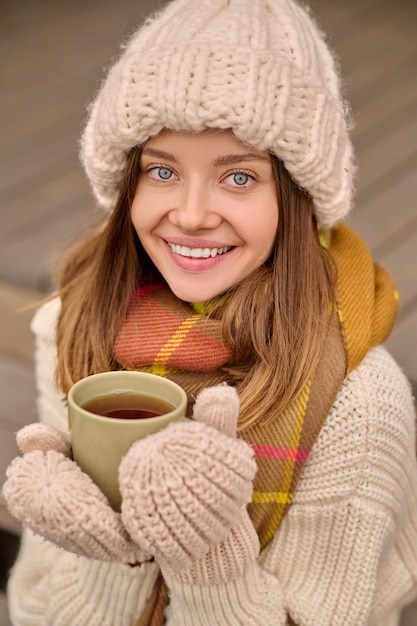 Femme tenant une tasse souriant à la caméra à l'extérieur
