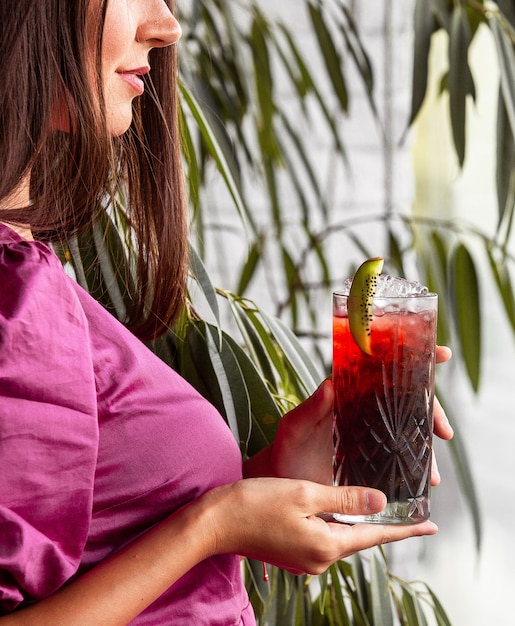 Femme tenant un verre de cocktail rouge garni de kiwis