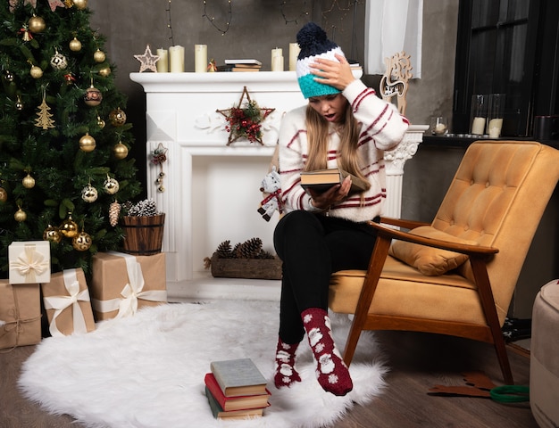 Femme en tenue d'hiver vérifiant les noms de livres près de la cheminée.