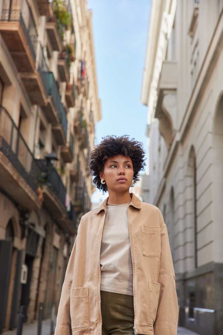 Photo gratuit une femme en tenue à la mode marche dans la rue près de bâtiments anciens regarde autour de elle profite de promenades en milieu urbain avec une zone publicitaire passe une belle architecture