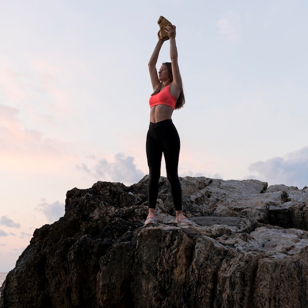 Femme en tenue de sport debout sur une côte avec ses bras vers le haut