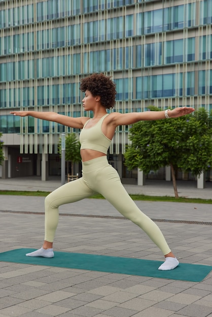 une femme en tenue de sport étire les bras pose sur un tapis de fitness se réchauffe avant l'entraînement en faisant des exercices dans le centre-ville en posture de guerrier