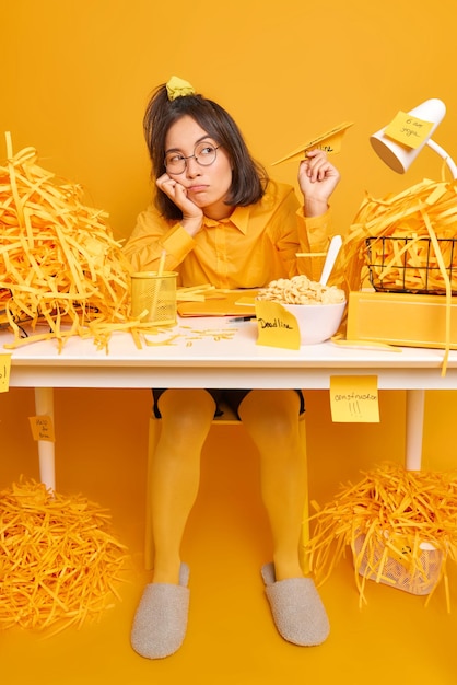 une femme tient un avion en papier en pleine réflexion pense aux futures poses de projets sur le bureau avec différentes choses autour isolées sur le jaune. Tir monochrome.