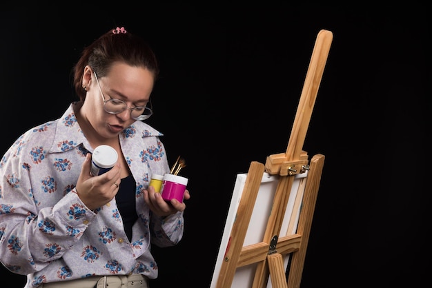 La femme tient la brosse et les peintures sur le noir