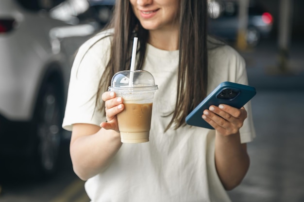 Photo gratuite une femme tient du café et un smarton dans ses mains dans un parking