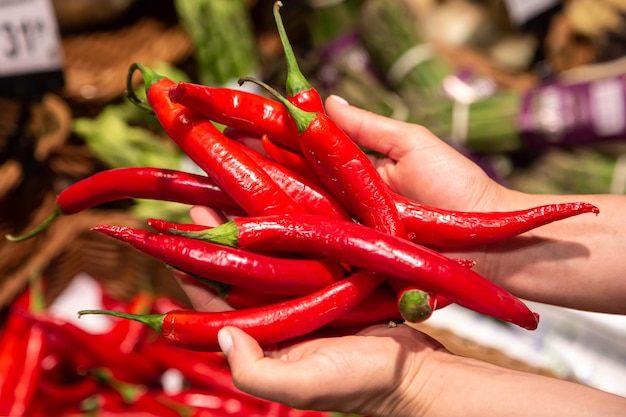 La femme tient du piment rouge dans le magasin ou sur le marché en gros plan