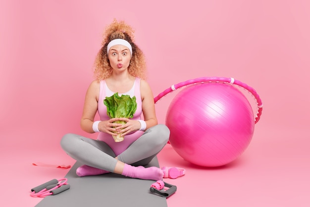 Photo gratuite une femme tient un légume vert a une alimentation saine et un mode de vie actif est assise les jambes croisées sur des exercices de tapis de fitness à la maison