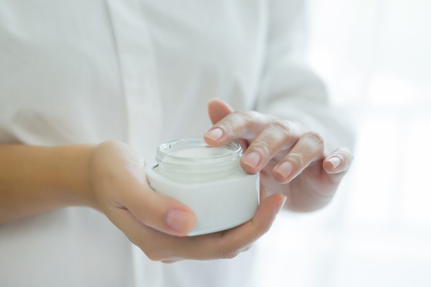 femme tient un pot avec une crème cosmétique dans ses mains