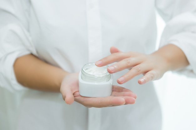 femme tient un pot avec une crème cosmétique dans ses mains