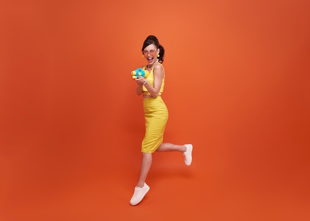 Femme de tourisme sautant voyageant avec un pistolet à eau pendant le fond du studio du festival de Songkran