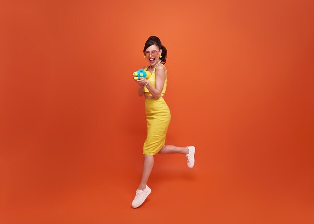 Femme de tourisme sautant voyageant avec un pistolet à eau pendant le fond du studio du festival de Songkran