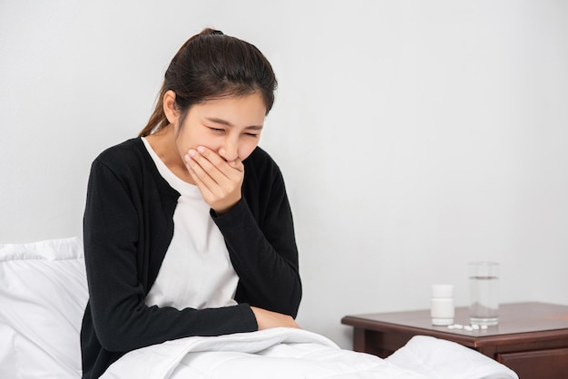 Photo gratuite la femme toussa et couvrit sa bouche avec sa main et s'assit sur le lit.