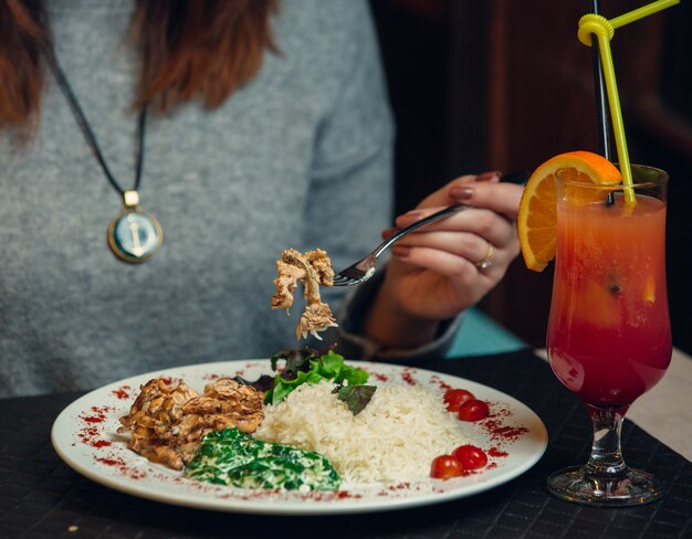 Femme en train de dîner avec du riz, des herbes et un verre de jus d'orange rouge.