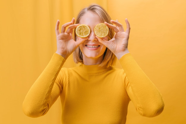 Photo gratuite femme avec des tranches de citron devant les yeux dans une scène jaune