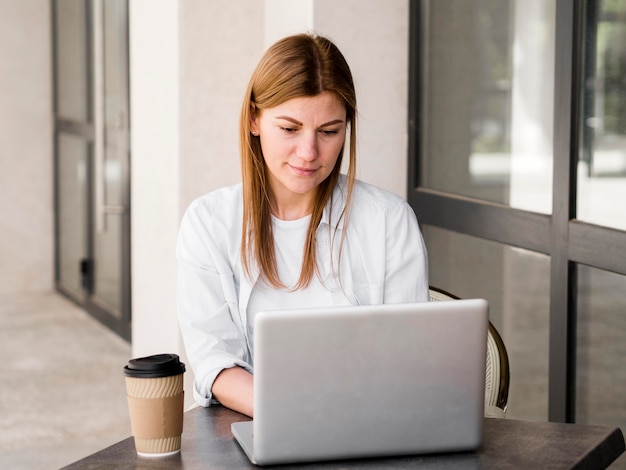 Femme travaillant sur un ordinateur portable à l'extérieur tout en buvant un café