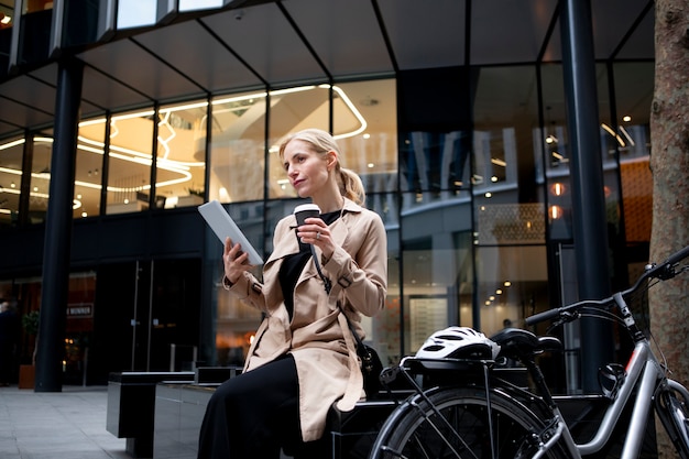 Femme travaillant sur sa tablette à l'extérieur et buvant du café