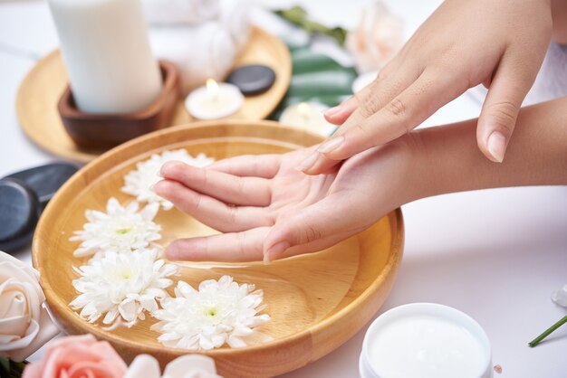 Photo gratuite femme trempant ses mains dans un bol d'eau et de fleurs, traitement spa et produit pour pieds féminins et spa pour les mains, galets de massage, eau de fleurs parfumées et bougies, détente. mise à plat. vue de dessus.