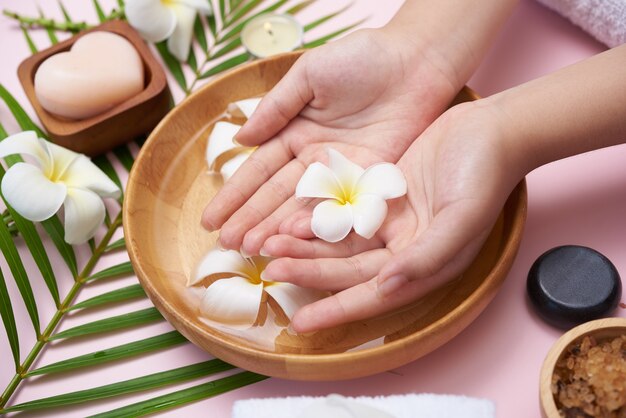 Femme trempant ses mains dans un bol d'eau et de fleurs, Traitement Spa et produit pour pieds féminins et spa pour les mains, galets de massage, eau de fleurs parfumées et bougies, Détente. Mise à plat. vue de dessus.