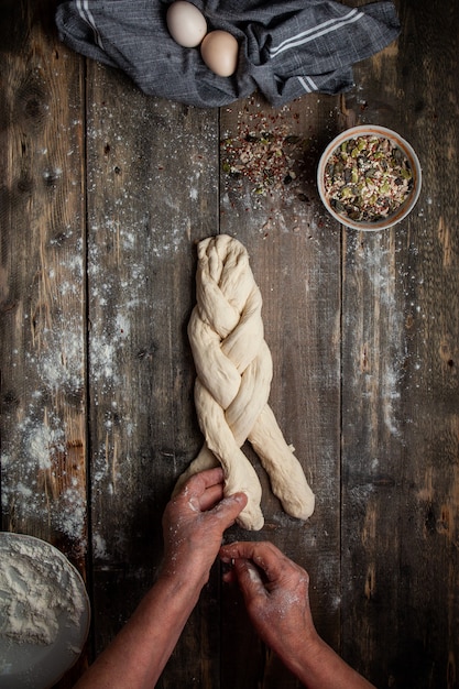 Femme tressant la pâte avec les mains sur la vue de dessus de table en bois