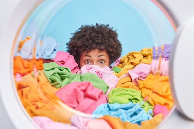 Une femme troublée et choquée se cache derrière un gros tas de linge surchargé de tâches ménagères et de responsabilités domestiques regarde les yeux égarés pose du tambour de la machine à laver