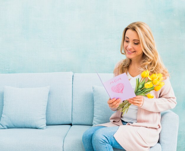 Femme avec des tulipes souriantes et lisant une carte postale pour la fête des mères