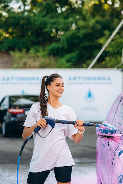 Femme avec tuyau haute pression en voiture recouverte de mousse rose