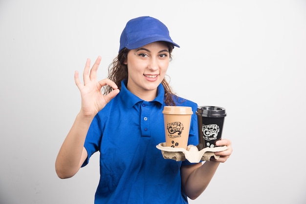 Photo gratuite femme en uniforme bleu montre le geste ok avec deux tasses de café sur fond blanc