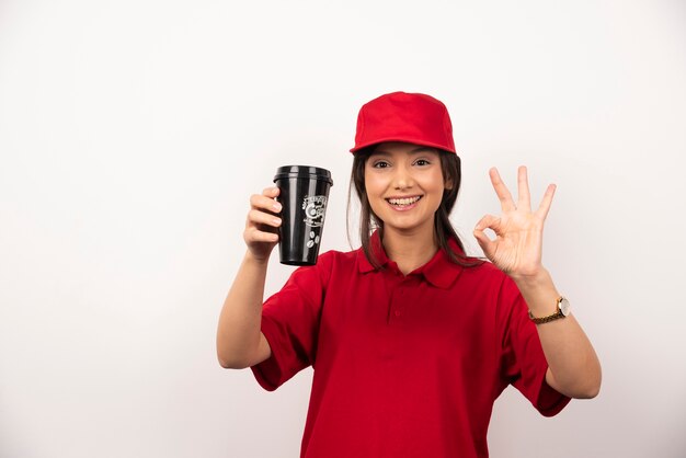 Femme en uniforme rouge montrant une tasse de café sur fond blanc.