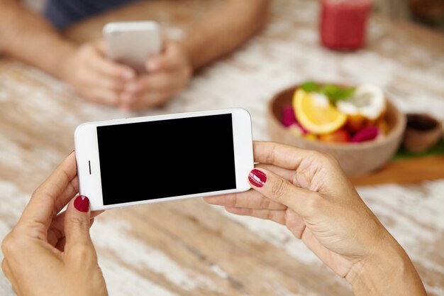 Femme utilisant une application en ligne pour éditer ses photos avant de les publier via un réseau social tout en se détendant au café