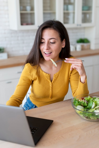 Femme utilisant un ordinateur portable et mangeant une salade