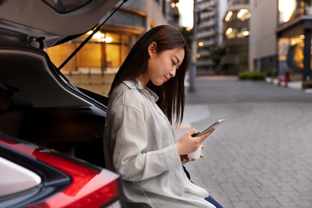 Photo gratuite femme utilisant son smartphone pendant la charge de la voiture électrique