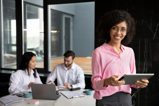 Femme utilisant une tablette pour travailler pendant que ses collègues utilisent un ordinateur portable