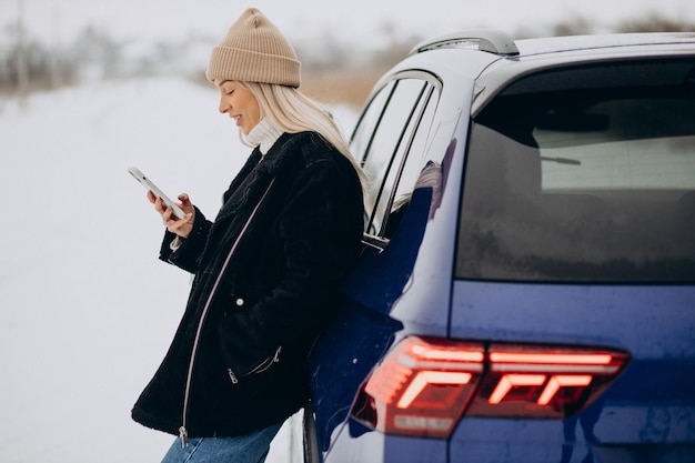 Femme utilisant un téléphone à l'extérieur de sa voiture dans un parc d'hiver