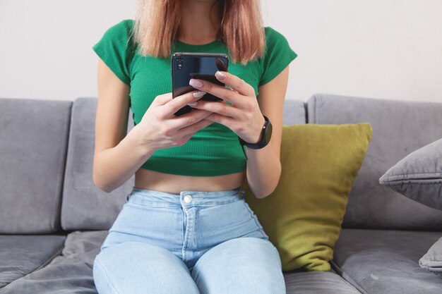 Femme utilisant un téléphone portable alors qu'elle était assise sur un canapé à la maison.