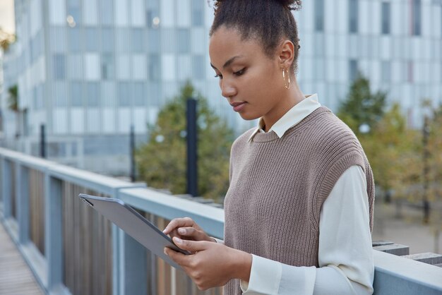 une femme utilise une tablette dans des poses de rue sur un pont lit un livre en ligne ou vérifie les flux sur les réseaux sociaux via wifi concentré à l'écran parcourt les pages du site Web