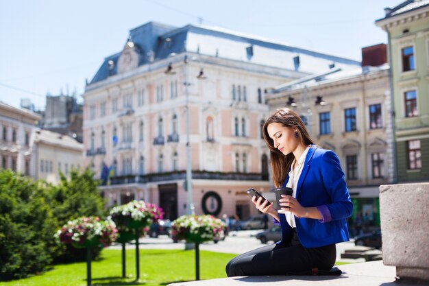 Femme vérifie son téléphone assis avec une tasse de café dans la rue