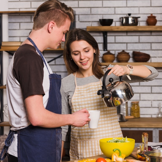 Femme versant de l&#39;eau de la bouilloire dans une tasse pour homme