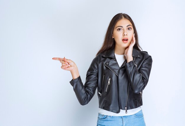 femme en veste de cuir pointant vers quelque chose sur le côté gauche.