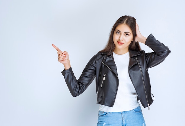 femme en veste de cuir pointant vers quelque chose sur le côté gauche.