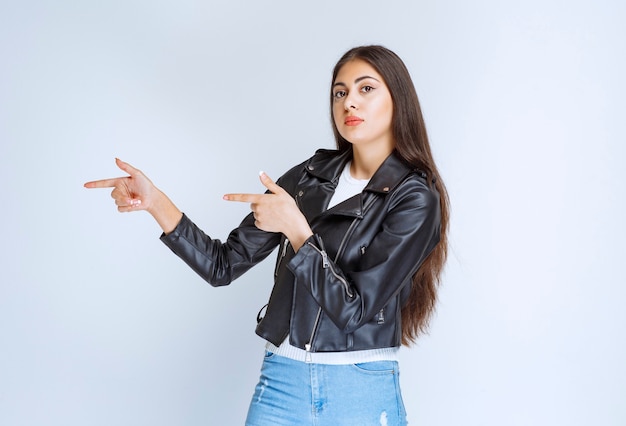 femme en veste de cuir pointant vers quelque chose sur le côté gauche.