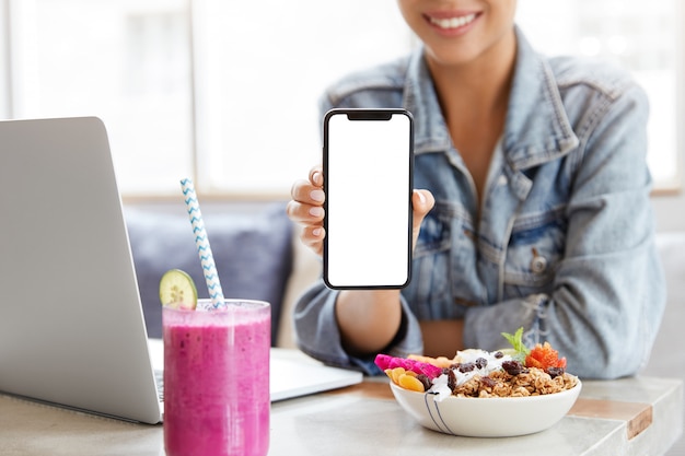 Femme en veste en jean élégante dans un café avec écran de smartphone vierge