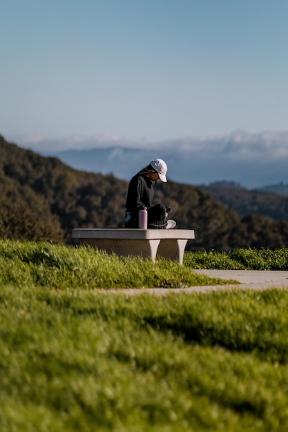 Femme en veste noire assise sur un banc de béton gris pendant la journée