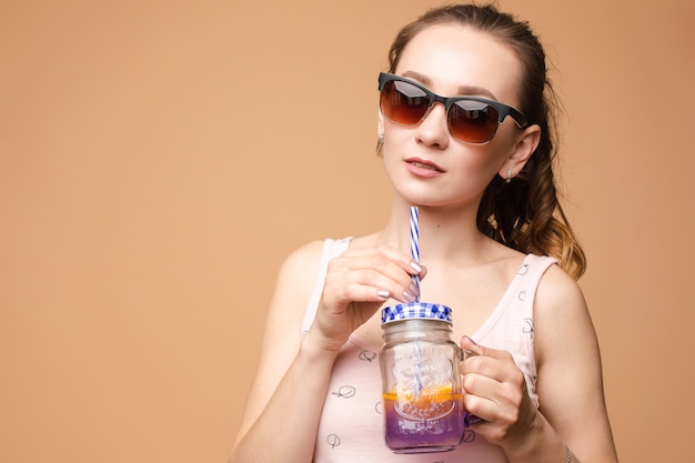 Une femme en vêtements clairs, un t-shirt et un short en jean, tient de la limonade froide dans ses mains sur un fond isolé